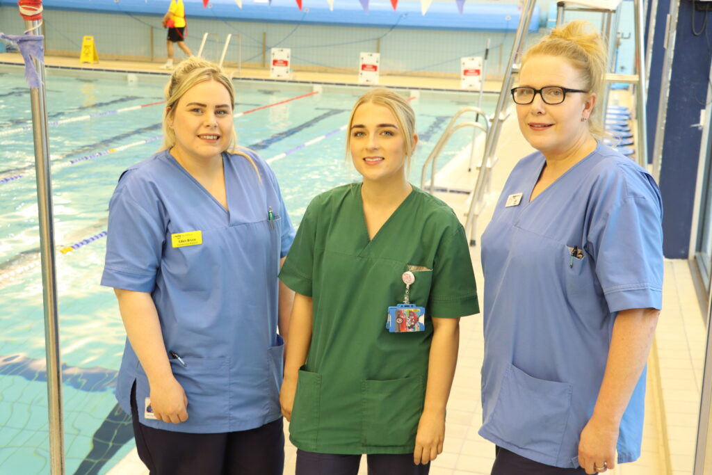 Thee nurses stand in front of a pool.