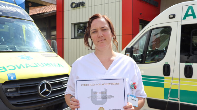 Lois Prest stands outside A&E. She holds a certificate.